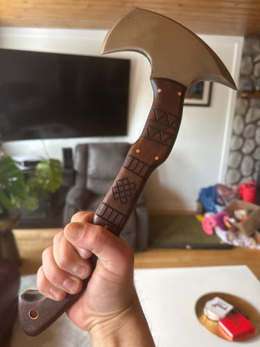 Reviewer holding a tomahawk with a detailed, engraved wooden handle in a living room setting.