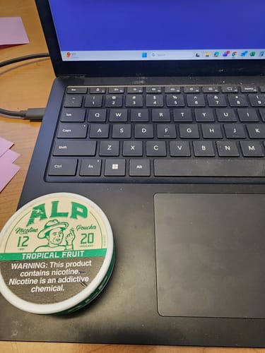 Customer's tin of ALP Tropical Fruit Nicotine Pouches resting on the touchpad of a black laptop.