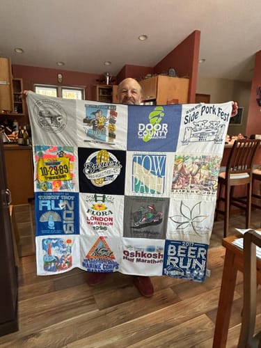 Customer proudly holding their large Project Repat T-Shirt Quilt made of t-shirts from various events and marathons.