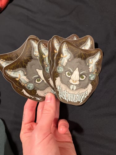 Customer holding a fan of glossy custom vinyl stickers featuring an illustrated, stylized cat-like creature.