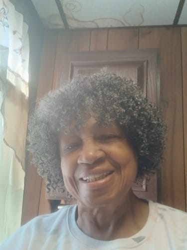 Reviewer smiling while wearing the short, curly BESSIE full wig.