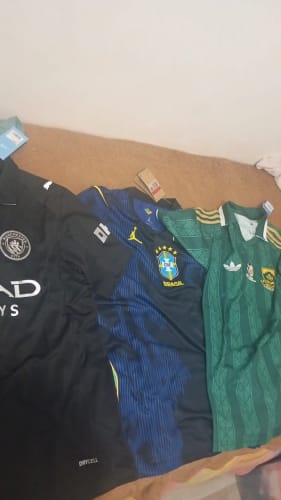 Le maillot Third 25/26 de Manchester City d'un client, posé à plat à côté de deux autres maillots de football.