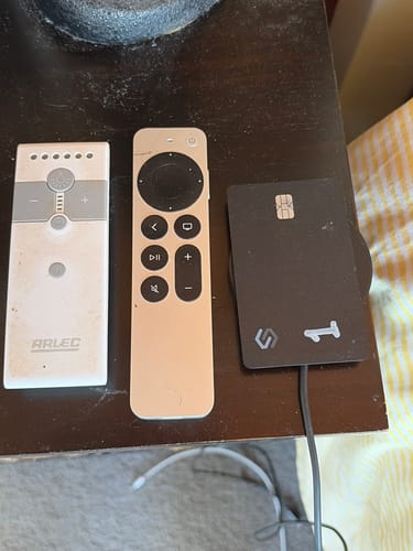 Reviewer's black, card-shaped SmartTag on a wooden table next to two remotes.