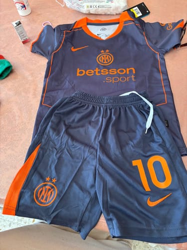 Cliente mostra il completo da bambino dell'Inter, con maglia e pantaloncini grigi con dettagli arancioni.