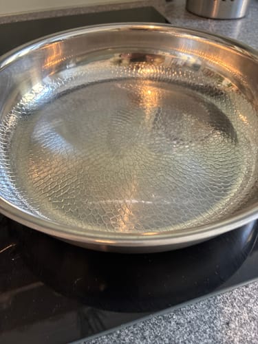 Rezensent zeigt eine Bratpfanne auf einem Induktionskochfeld. Sie hat eine strukturierte Oberfläche und ist leicht gewölbt.