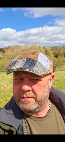 A reviewer wears their Donegal Touring Cap, showing the unique patchwork tweed design while outdoors on a sunny day.