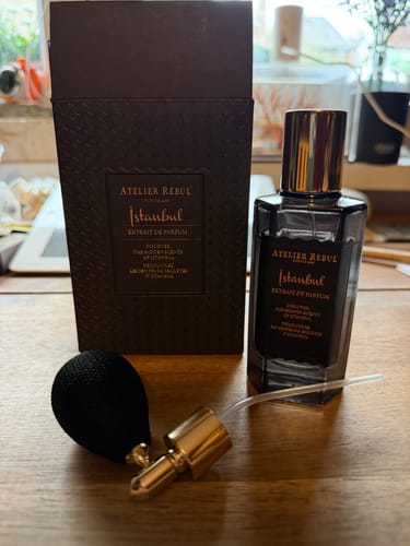 Recensent toont de Atelier Rebul Istanbul parfumfles met de doos en een losse verstuiver op een houten tafel.