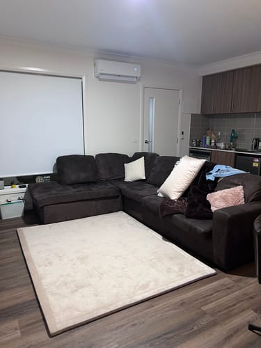 Customer's beige Mellow Mat on a dark wood floor in front of a sectional sofa.