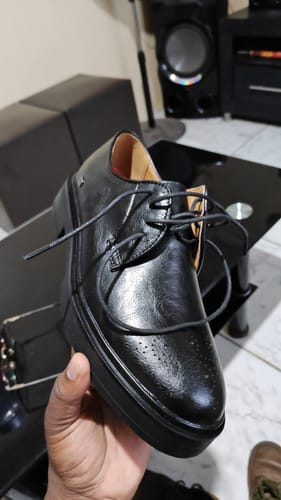 A customer holds up the black Mazerata Elia 4 leather shoe, showing its chunky sole and pin punch detail.