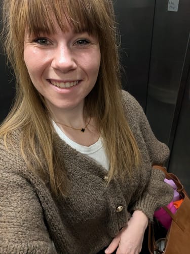 Kundin trägt das Überraschungsgeschenk, eine zarte Halskette mit einem kleinen, schwarzen Anhänger, zu einem Alltagsoutfit.