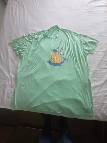 Cliente mostra a camisola Hamster verde-claro com estampa de um hamster dormindo, deitada na cama.
