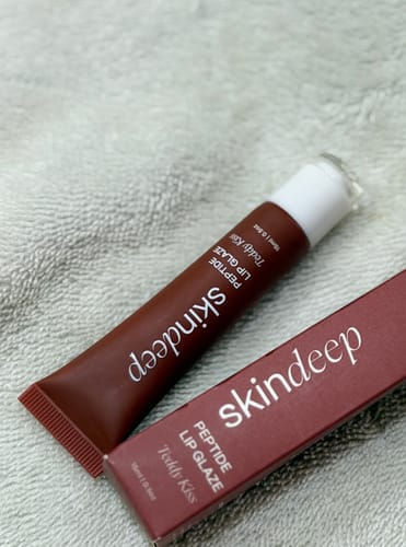 A reviewer's Peptide Lip Glaze in the Teddy Kiss shade, showing the product tube next to its box.