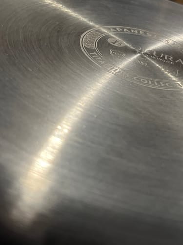 Rezensent zeigt eine Nahaufnahme des fehlerhaften Bodens einer Pfanne mit Metallrückständen.