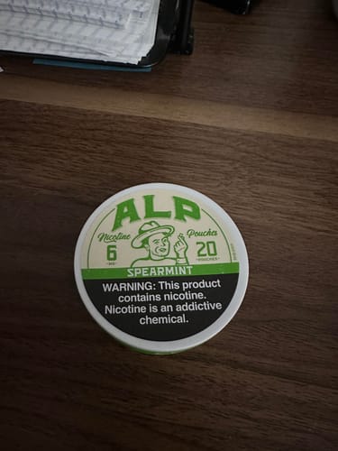 Customer's white and green tin of Spearmint Nicotine Pouches displayed on a wooden table.