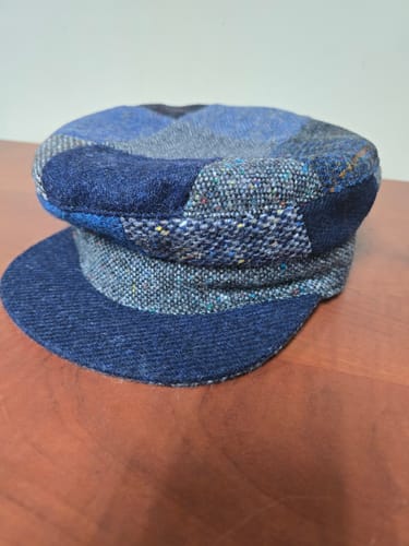Customer's blue patchwork Skipper Cap sitting on a wooden table, showing its unique tweed patterns.