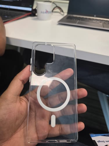A reviewer holds the Anti Yellow Magsafe Clear Case for Samsung, showing its transparent back and white magnetic ring.