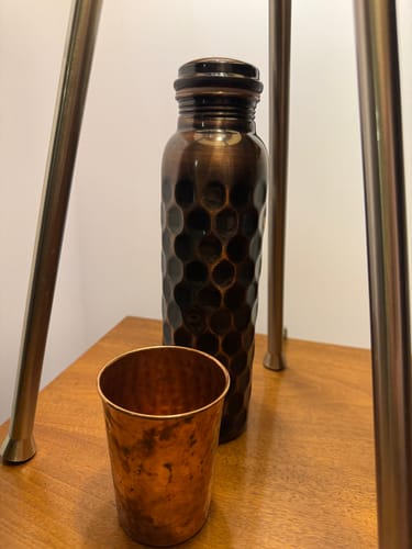 Reviewer's dark, hammered copper bottle and a matching glass from the set on a wooden table.