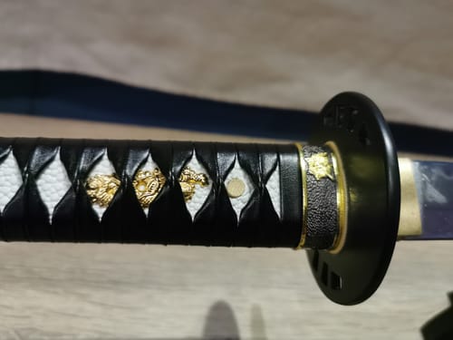 Customer's close-up of a katana hilt with a black wrap and golden ornaments.