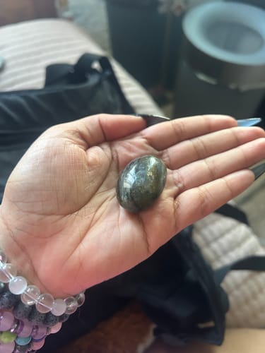Customer holding a dark, polished moonstone from the monthly crystal club in their palm.