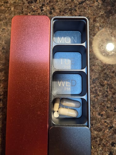 Reviewer's open gunmetal vitamin case with its metallic rose gold lid, showing pills in a compartment.