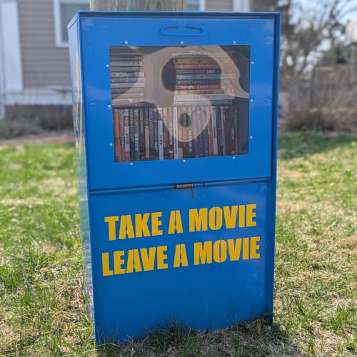 Reviewer's yellow custom vinyl decals applied to a blue movie library box, reading "TAKE A MOVIE LEAVE A MOVIE".