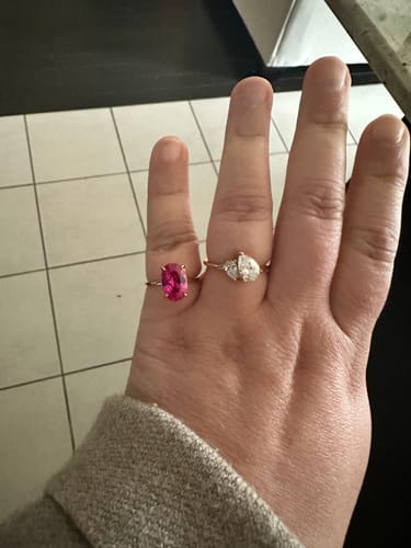 Customer's hand wearing the gold Leesha Ring, showing its two pear-cut stones next to another ring.