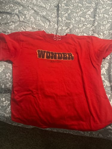 Customer's red wonder baby tee with a front graphic, laid out flat on a patterned surface.