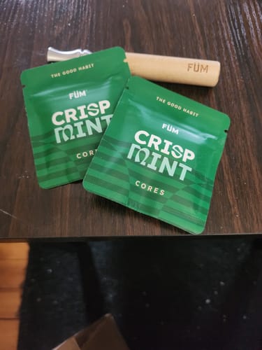 Customer's Füm device and two green packages of Crisp Mint Cores on a wooden table.