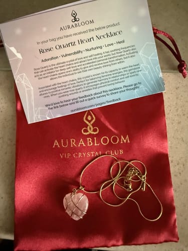 Reviewer's Rose Quartz Heart Necklace with a gold-colored chain, displayed on its red satin VIP Crystal Club pouch.