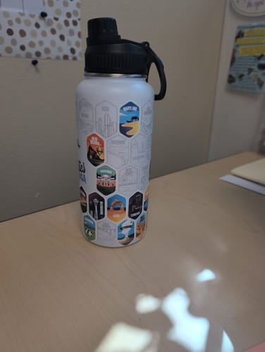 Reviewer's water bottle on a desk, showing the black Chug Lid with its handle and decorated with colorful stickers.