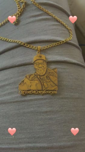 Customer's gold custom photo engraved pendant necklace featuring a man's portrait and an inscription, resting on a gray surface.