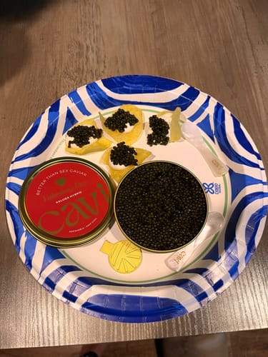 Customer's open tin of black caviar and prepared crackers on a paper plate for a Valentine's Day meal.