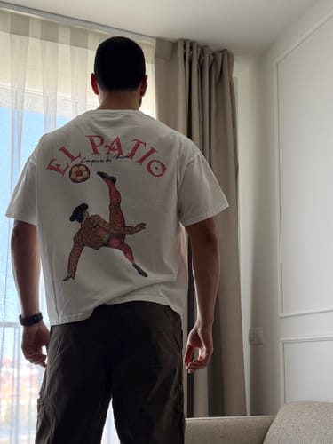 Customer seen from behind wearing the white LA CAMISETA: FOOTBALL t-shirt, showing the graphic print on the back.