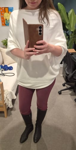 Reviewer shows the loose fit of the ivory Asymmetric Draped top in a mirror selfie.