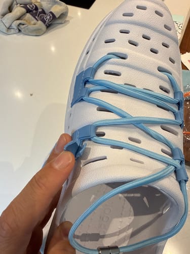 A customer's hand holds a white Wildpools shoe, showing a broken light blue plastic strap holder.