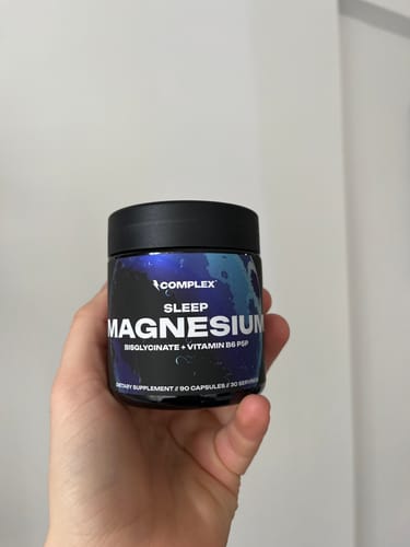 Customer holding the black jar of Sleep Magnesium supplement in their hand.