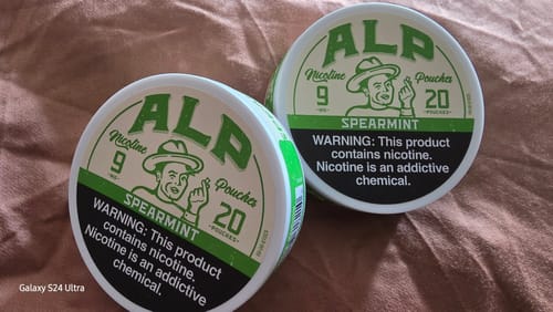 Customer's two tins of Spearmint Nicotine Pouches on a brown textured surface.