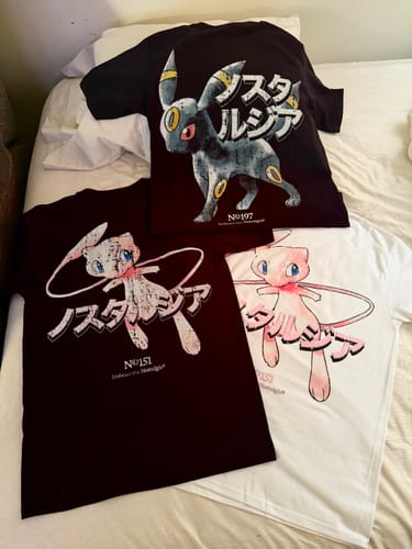Cliente muestra su camiseta negra Moonlight 197 junto a otras dos camisetas de estilo similar sobre una cama.