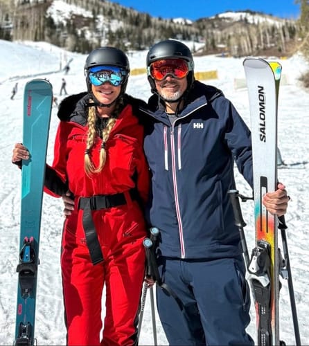 Reviewer wearing the red one-piece ski suit while posing with a companion on a snowy mountain.