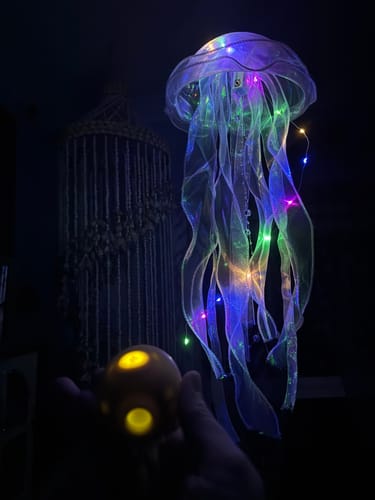 Customer's hand holding the glowing Lem Clitoral Massager in a dimly lit, creative room.