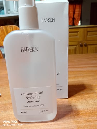A customer's white bottle of Bad Skin Collagen Bomb Hydrating Ampoule sits on a table next to its box.