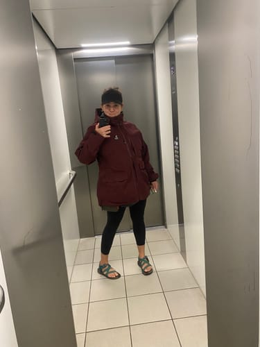 Kunde tager et spejlselfie iført den røde Pack&Carry Shell Jacket i en elevator.