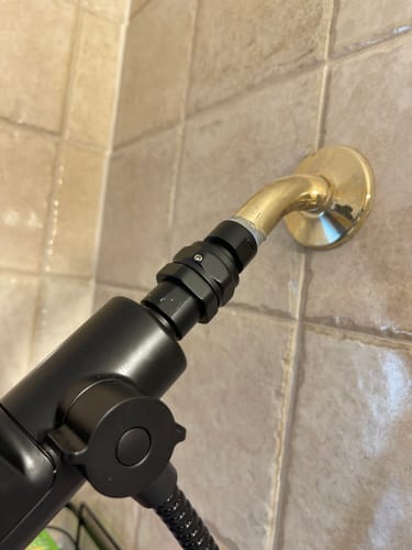 Customer's black Shower Head Swivel Adapter installed between a gold shower arm and a shower head.