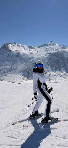 Reviewer on a snowy mountain wearing the white and black faux fur one-piece ski suit.