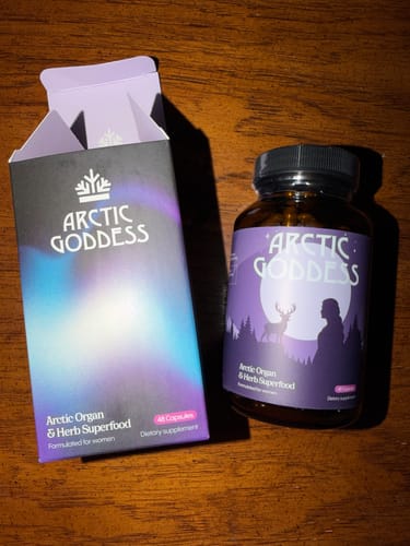 Customer's bottle of Arctic Goddess Reindeer Organ Superfood next to its open, purple box on a wooden surface.
