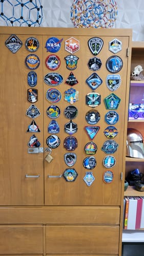 Reviewer's Artemis II - Collectors Patch displayed with a large collection of space-themed patches on a wooden cabinet.