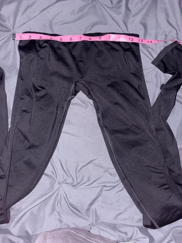 A customer's black Seamless LowRise Leggings laid flat on a bed with a pink tape measure across the waistband.