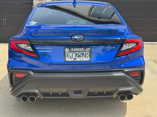 Reviewer's black TUNA NO CRUST LICENSE PLATE FRAME installed on the back of a blue car.
