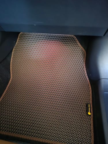 Recenzent pokazuje brązowy dywanik samochodowy na zamówienie, zainstalowany po stronie pasażera.