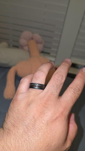 Customer wearing a black ring with a textured meteorite and dinosaur bone inlay on their hand.